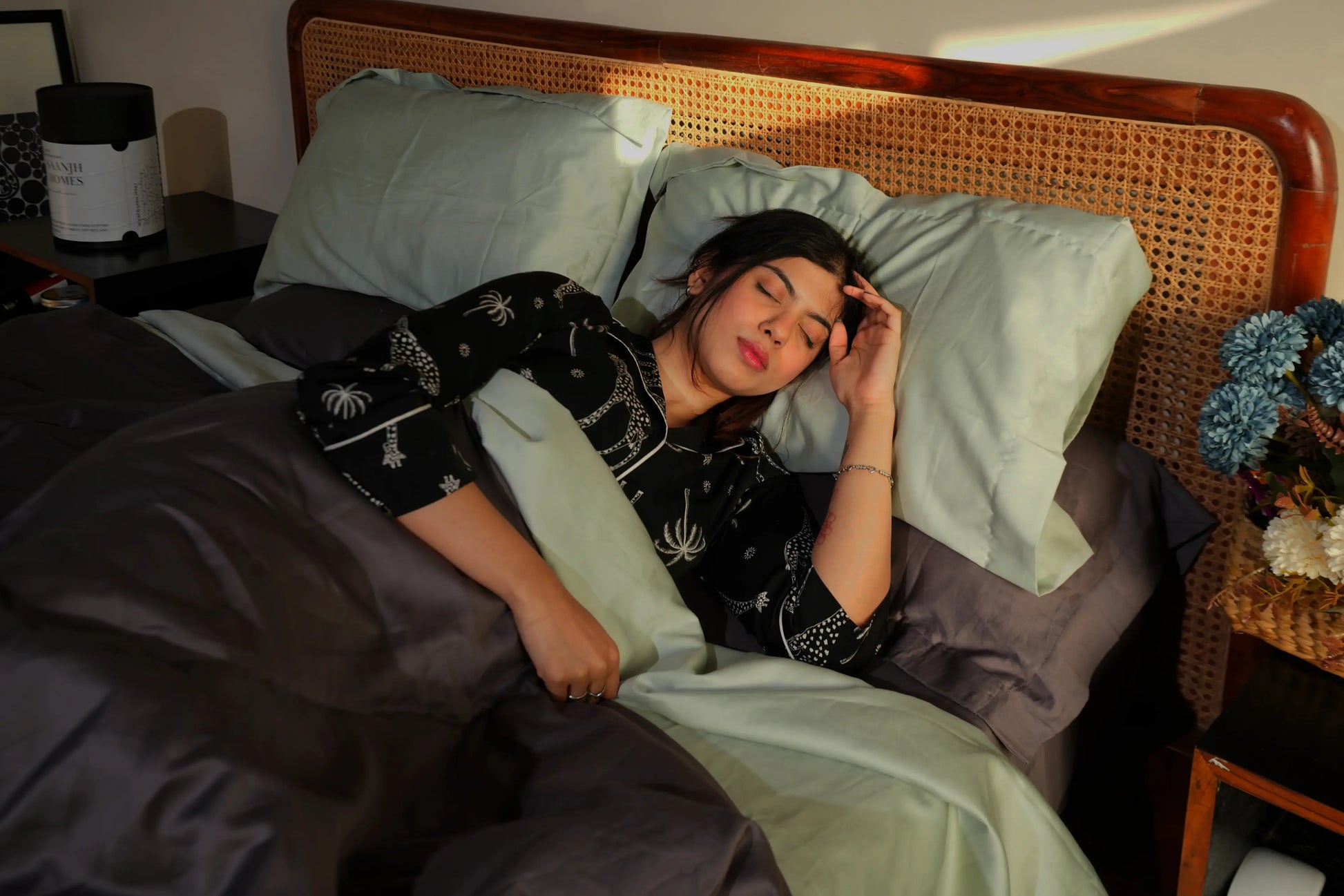 Woman lying in bed with ash sheets , mint pillows and a wicker headboard.
