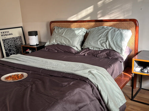 Bedroom with a bed featuring green and grey bedding, a nightstand, and a side table.
