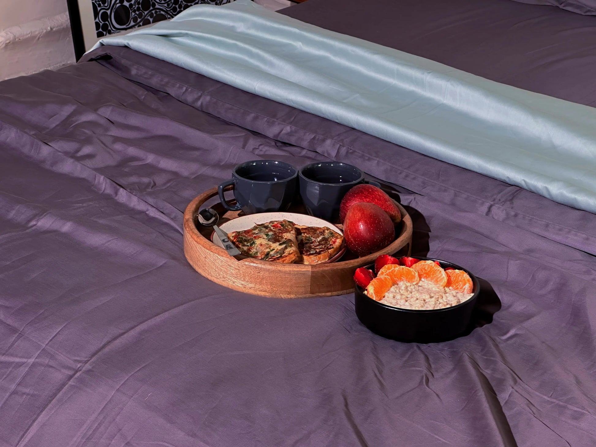 Tray with pizza, cups, and fruit on a bed