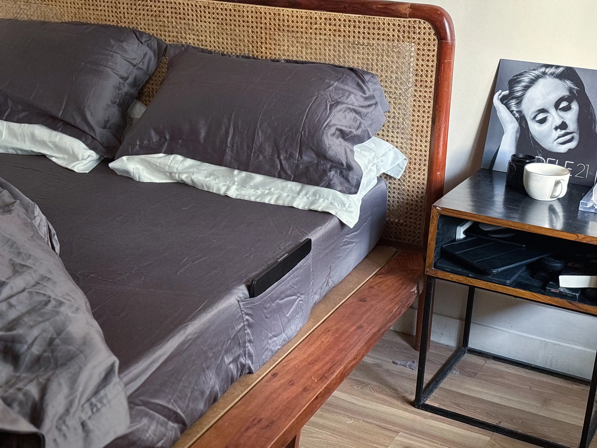 Bed with gray bedding and pillows next to a nightstand with a cup and photo frame.