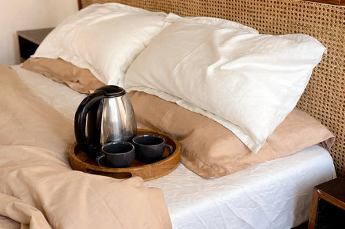 Bed with white sheet, beige pillows, and a tray with a coffee pot and cups.