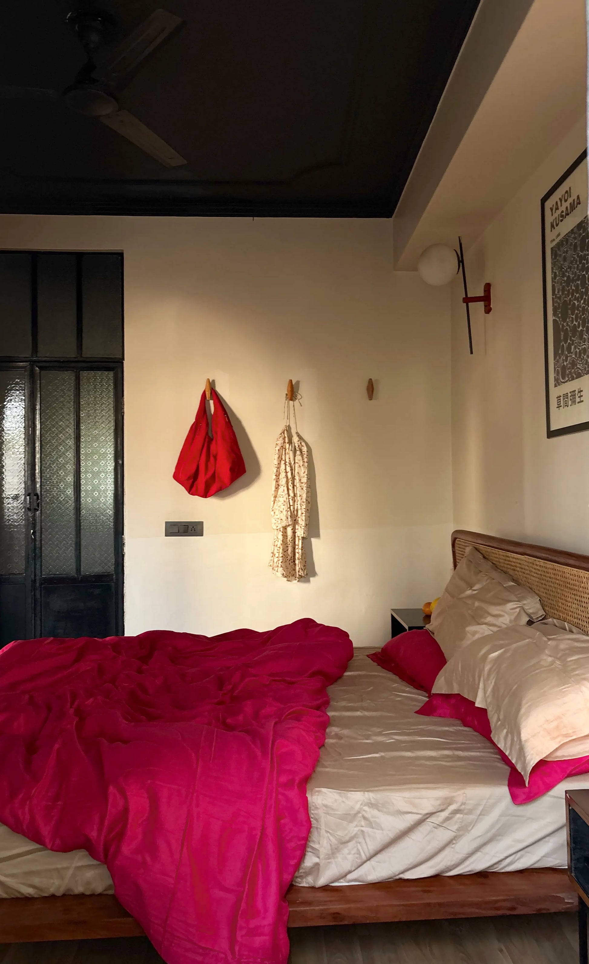 Bedroom with pink blanket and red bed and white dress hanging on the wall