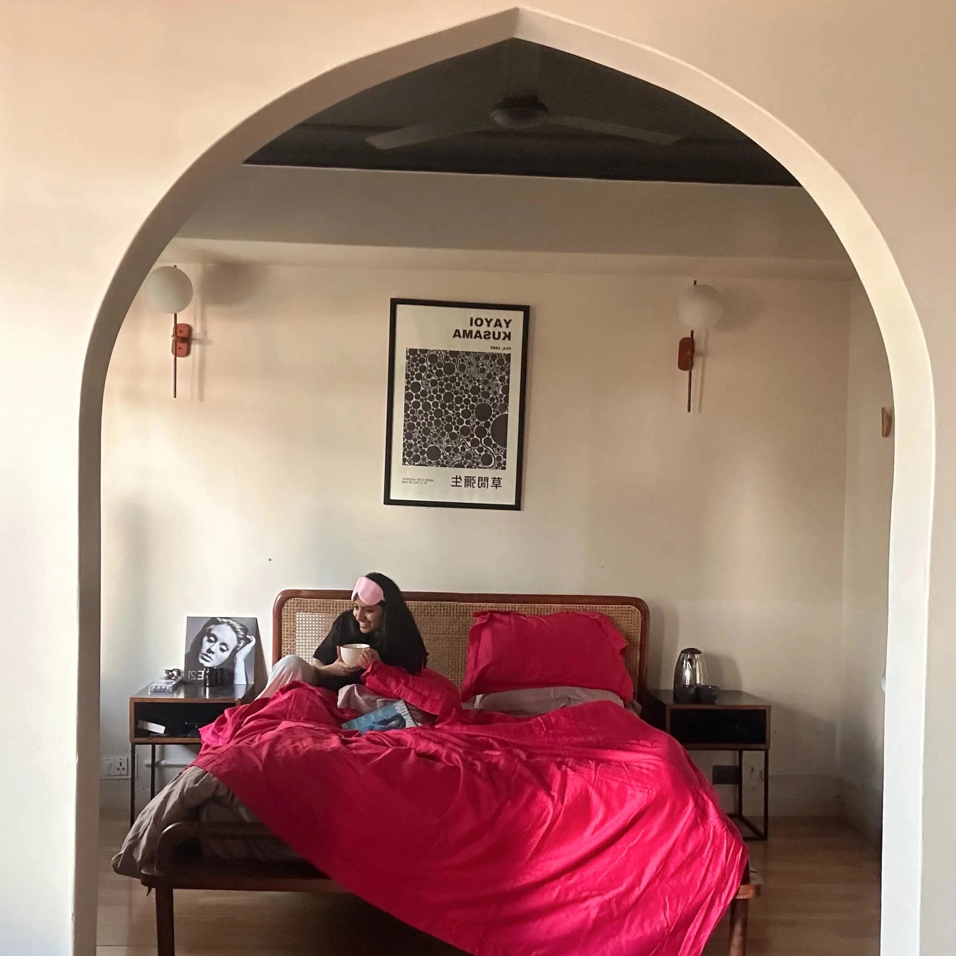 Person lying on a bed with pink bedding in a room with an archway.