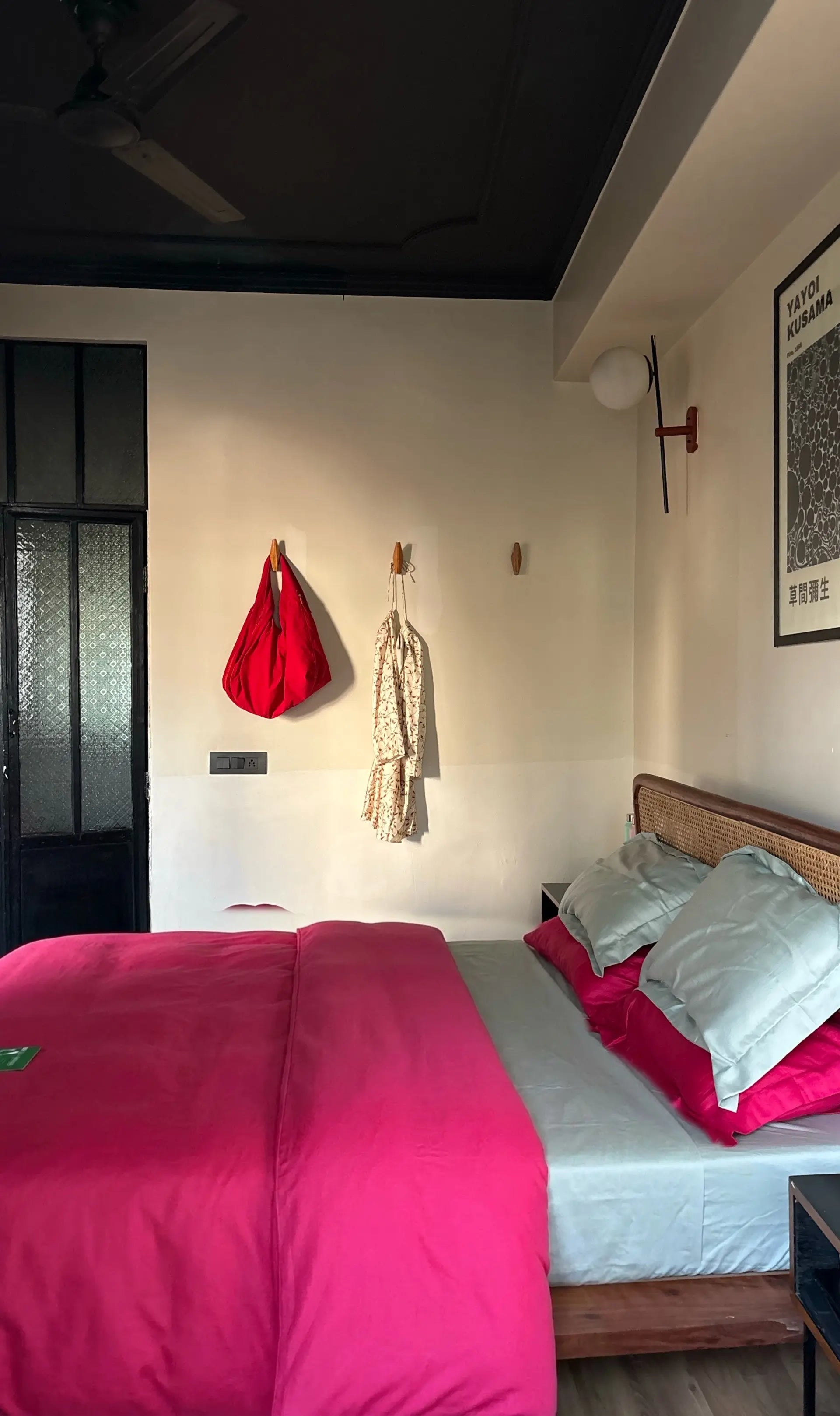 Bedroom with pink bedding, white pillows, and a red bag hanging on the wall.