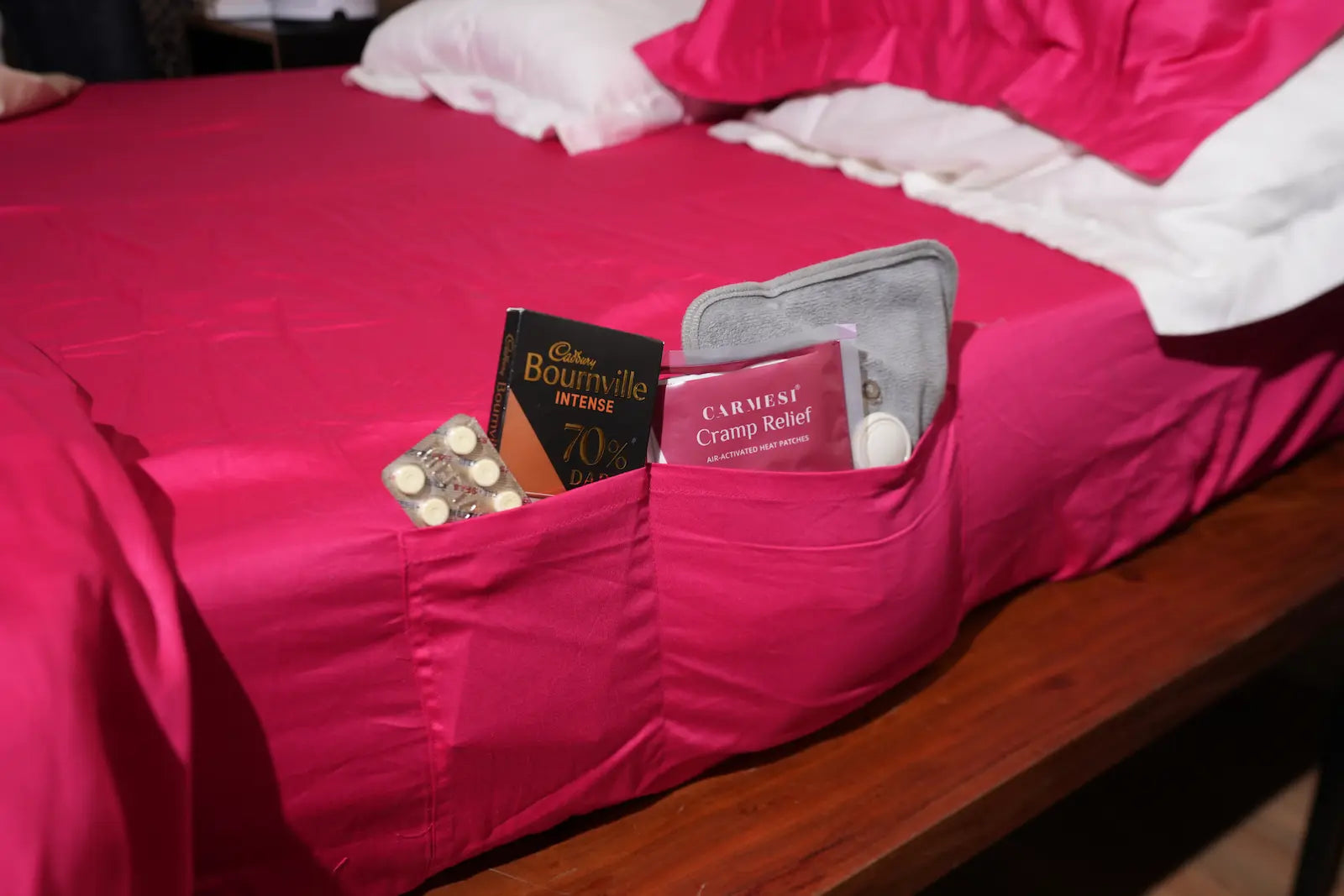 Pink pocket on a bed with period kit. Pads, heating pad, cramp relief, meds