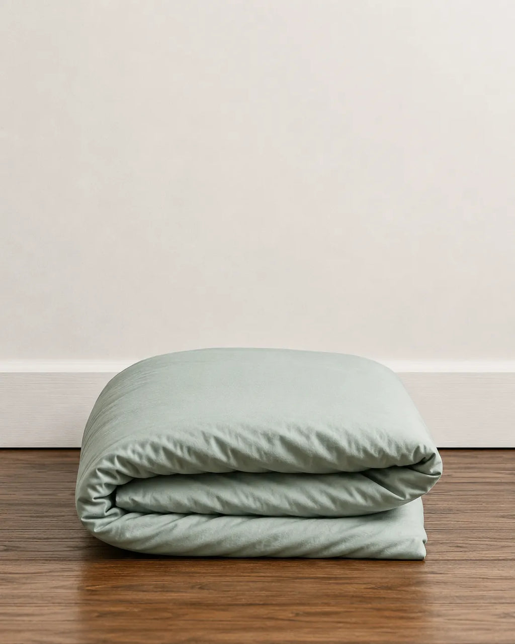 A folded saanjh mint duvet sits on a dark wood floor against a plain off-white wall.