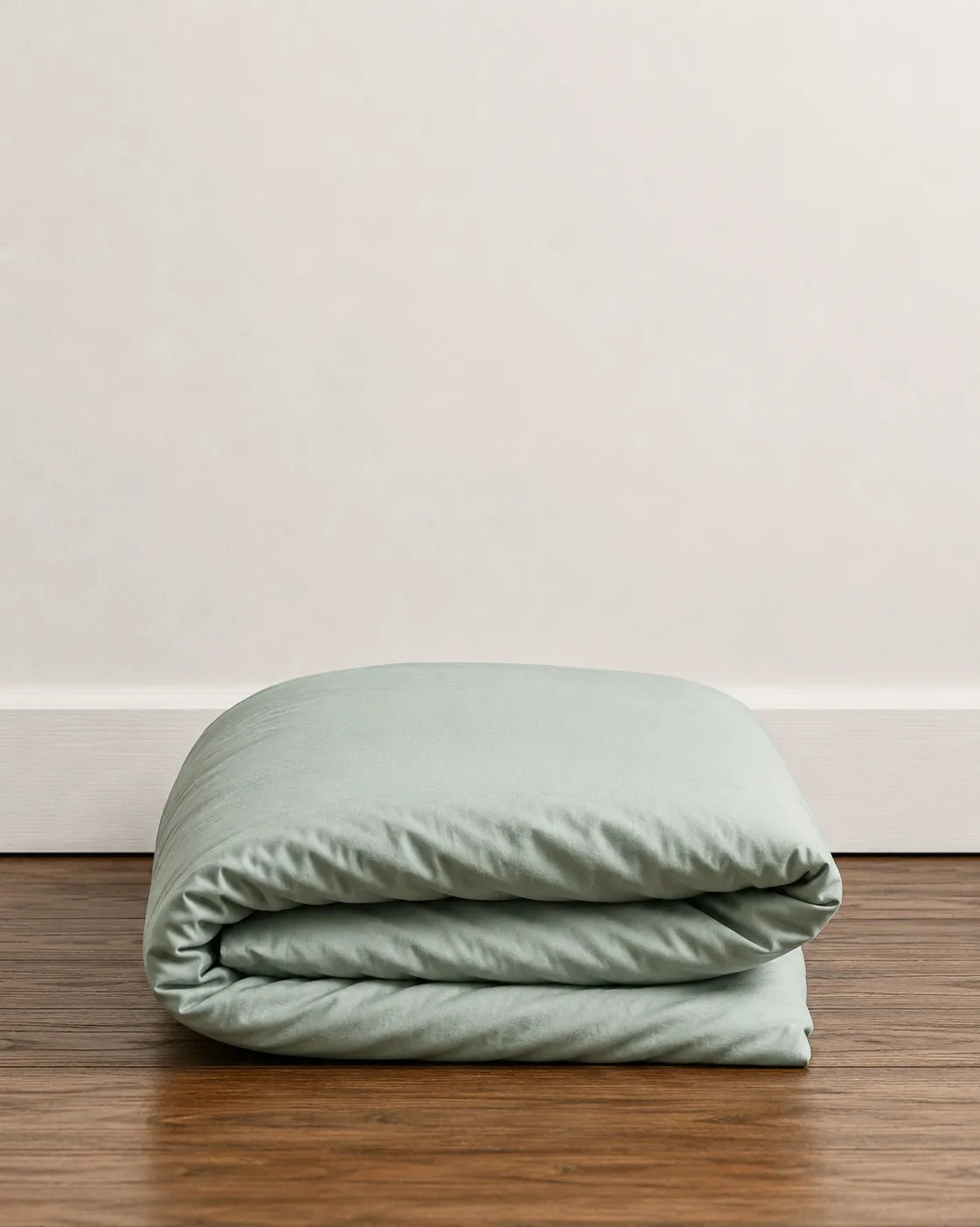 A folded saanjh mint duvet sits on a dark wood floor against a plain off-white wall.