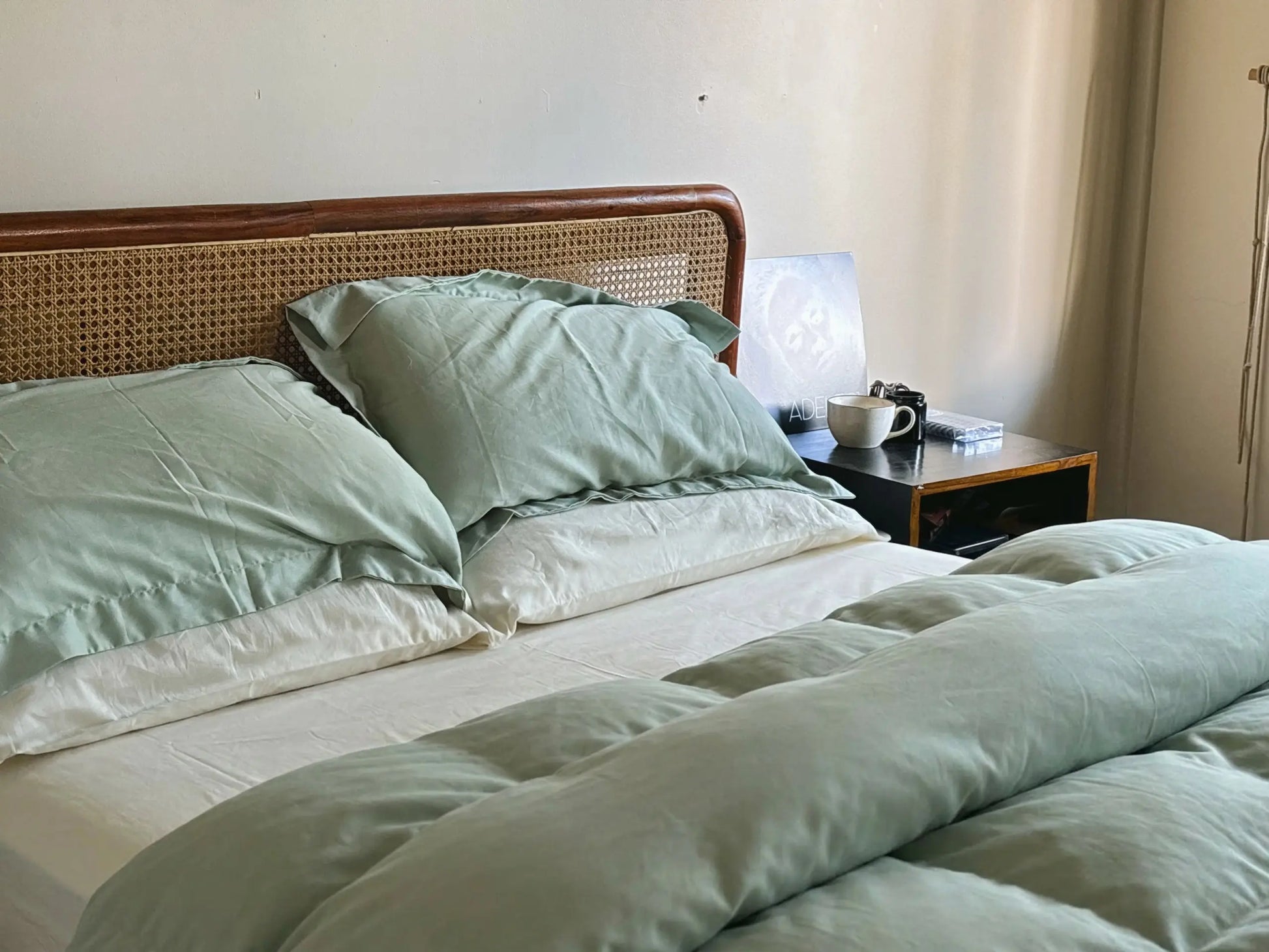 Bed with green bedding and a wooden headboard, nightstand with lamp and cup.