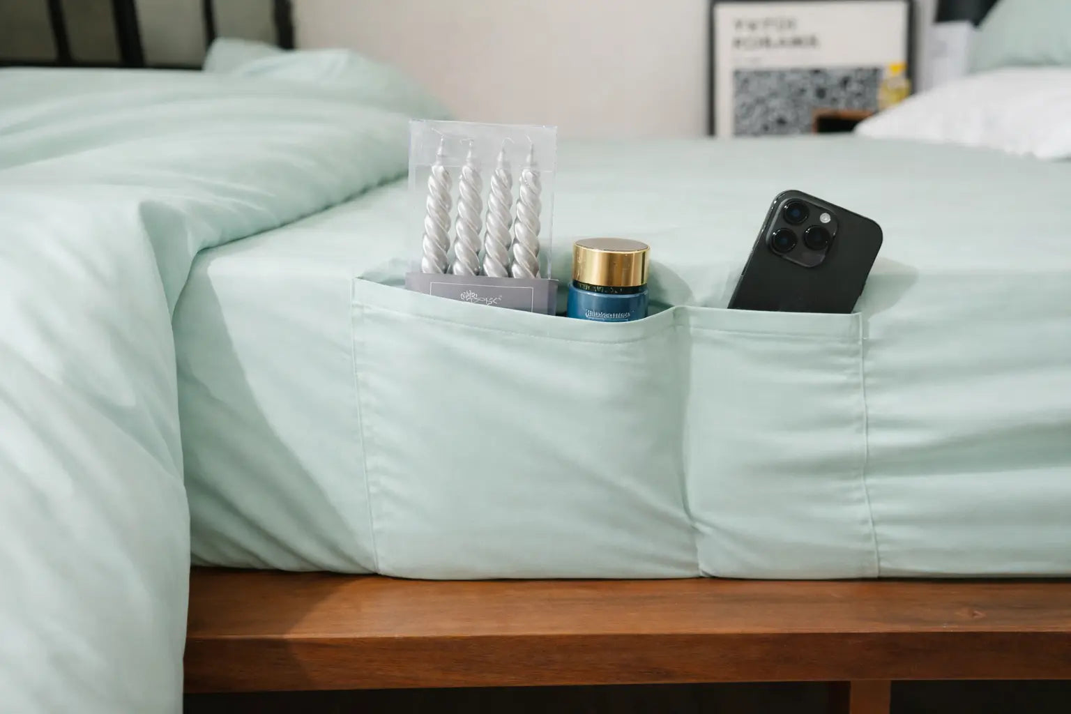 mint sheet with built-in pockets holding a phone, bottle, and other items on a bed.