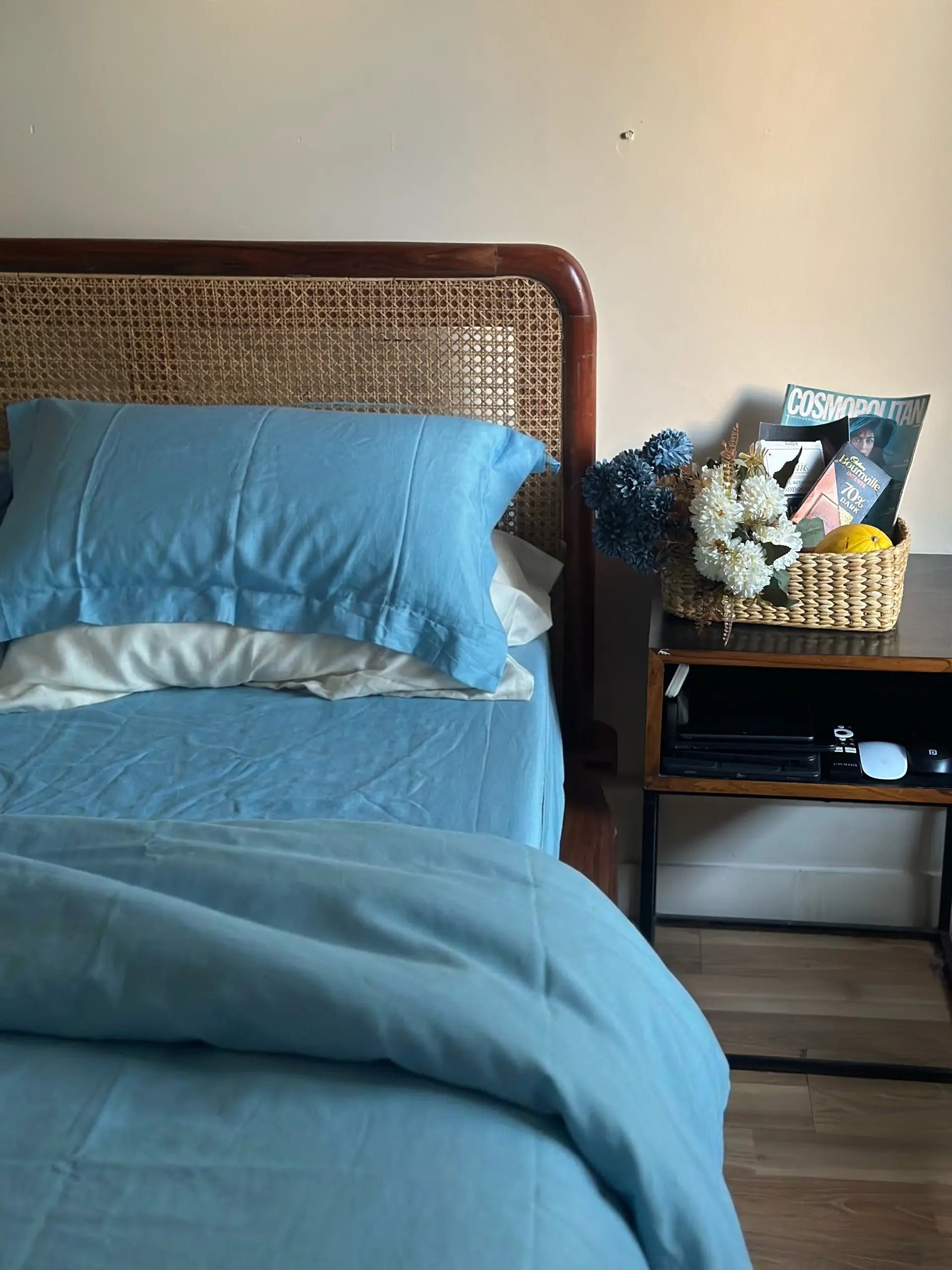 Bed with blue bedding and pillows, nightstand with decorative items, and wicker headboard.