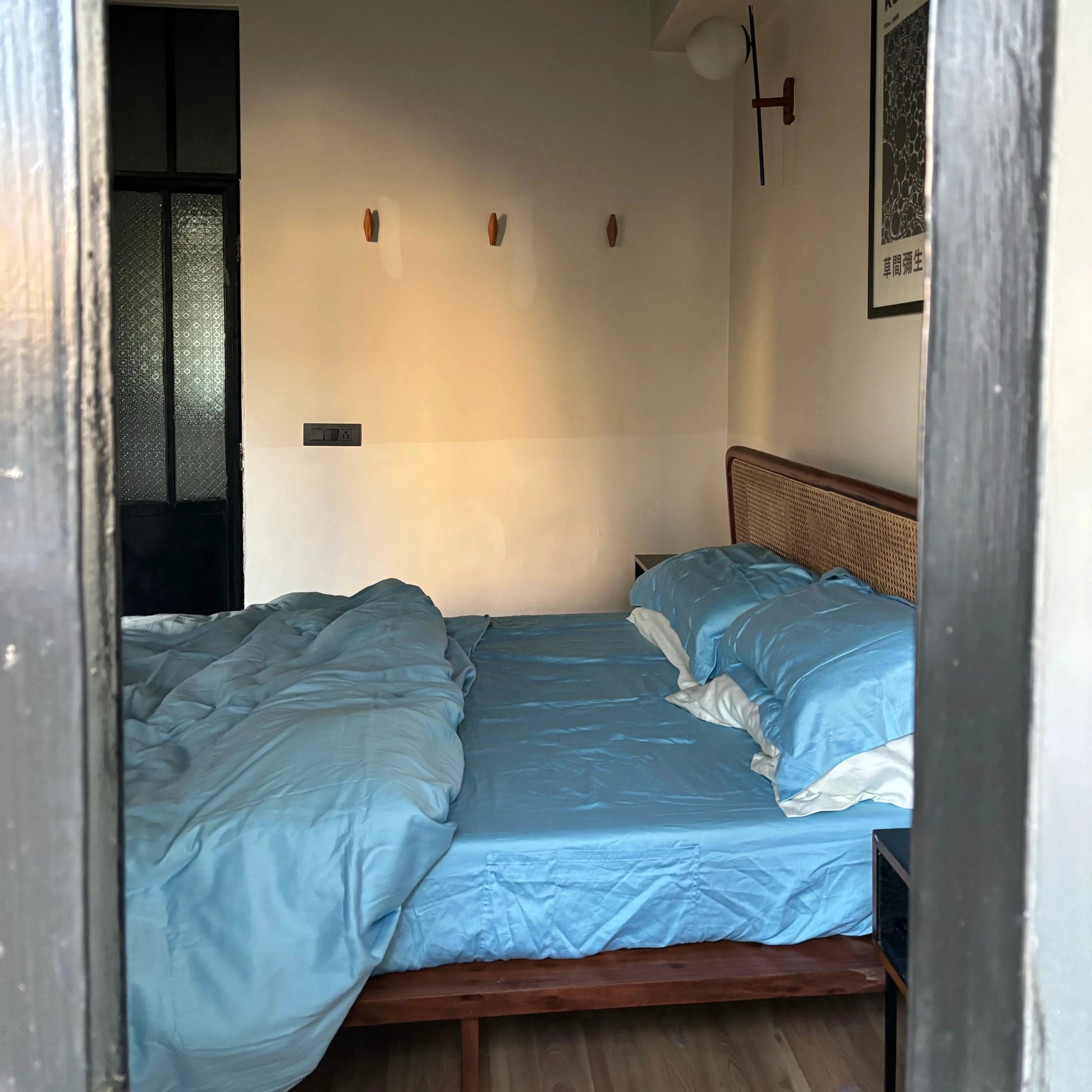Bedroom with a bed covered in blue bedding, wooden headboard, and wall-mounted lamps.