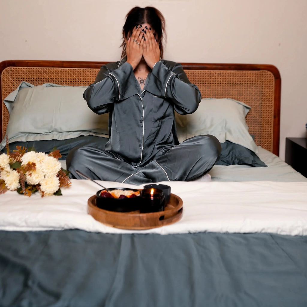 Person in pajamas sitting on a bed with a tray of food and flowers.