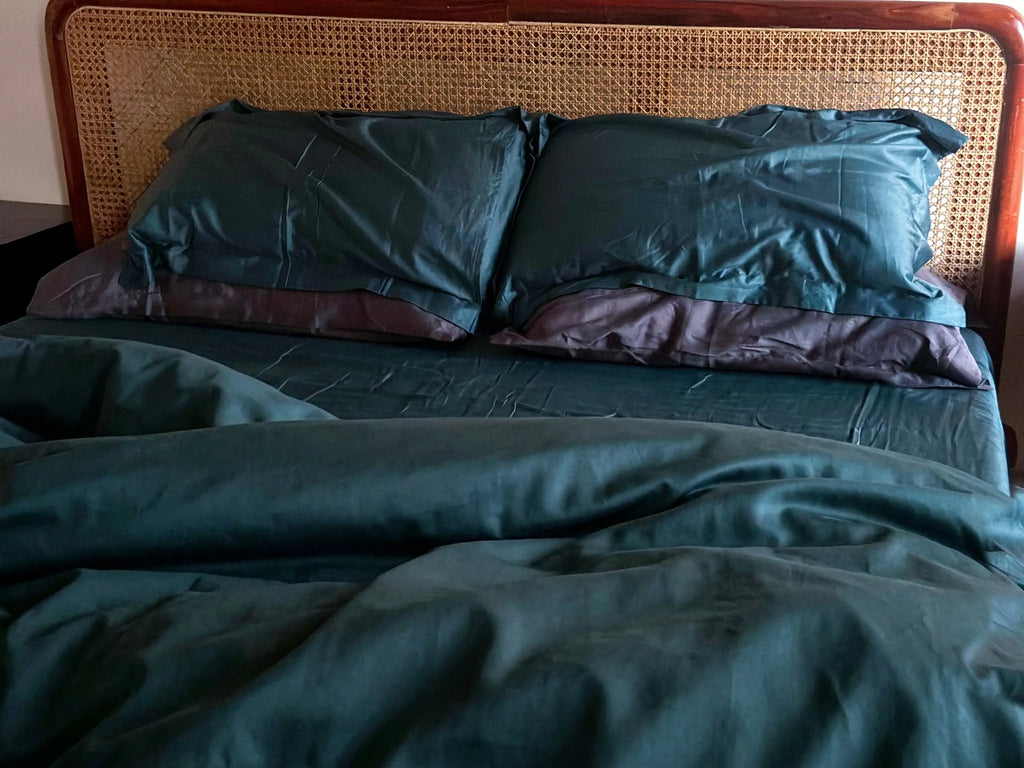 Bed with teal bedding and pillows against a wooden headboard