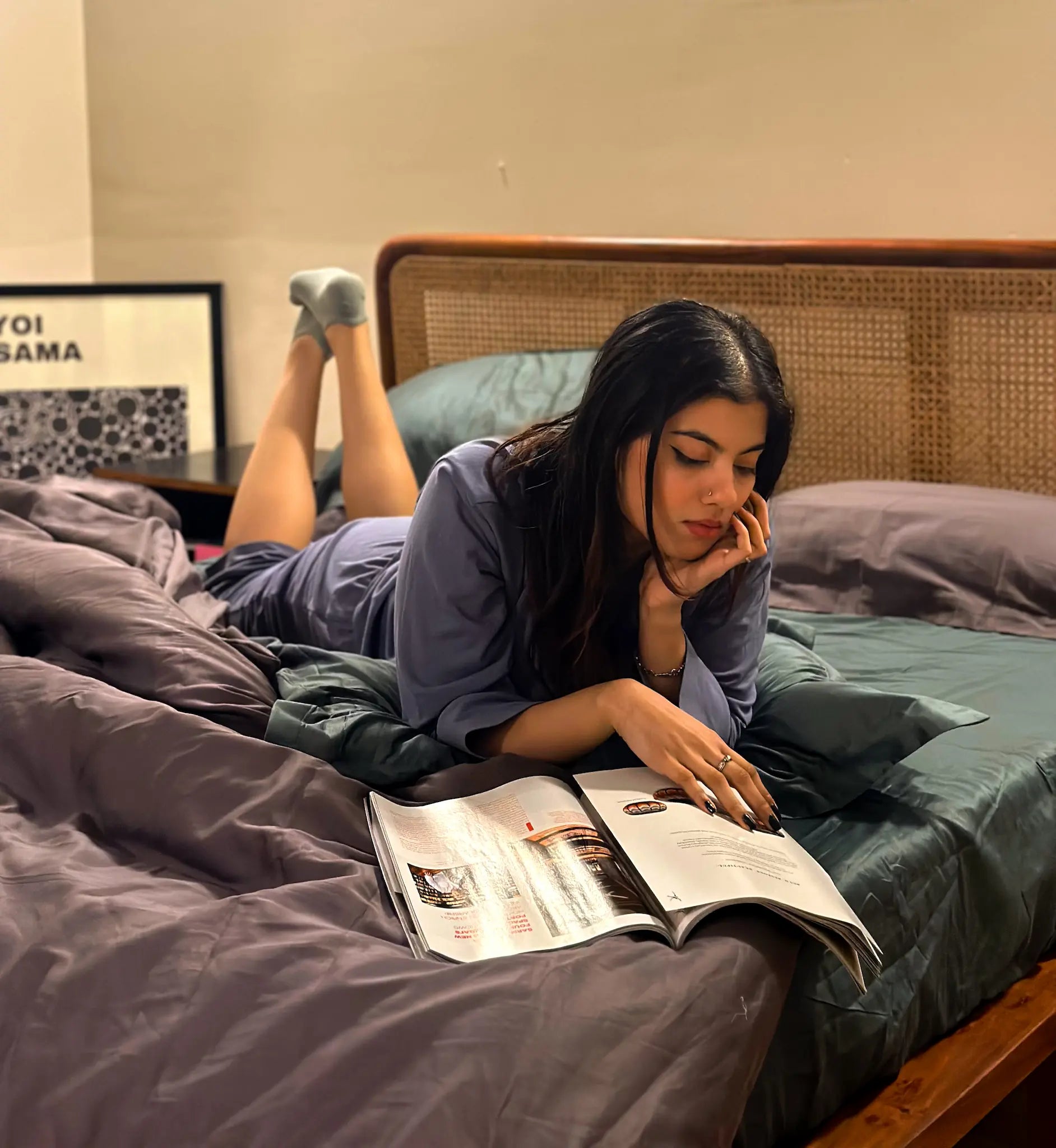 Woman lying on a bed reading a magazine in a bedroom setting.