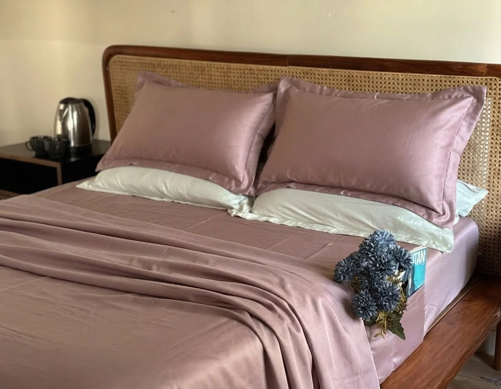 Bed with pink cotton sheets and pillows in a bedroom setting.
