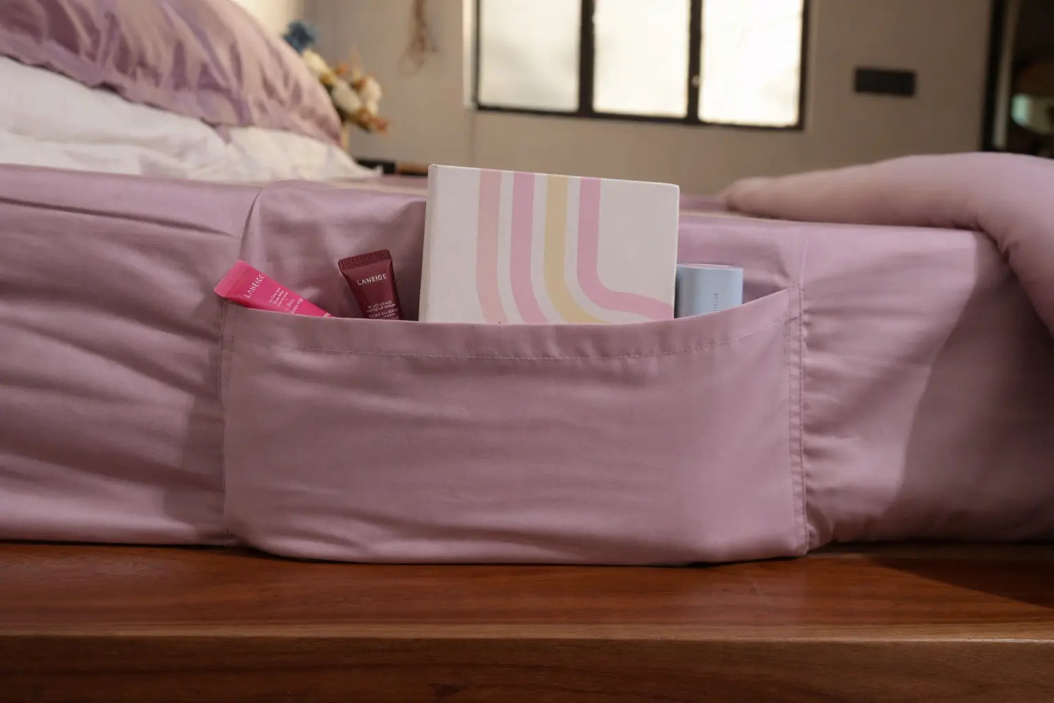 Pink saanjh pocket on a bed with everyday items inside, in a bedroom setting.