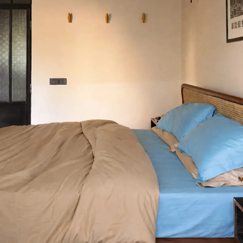 Bedroom with a bed featuring blue bedding and beige blanket, wall-mounted lamps, and a framed picture.
